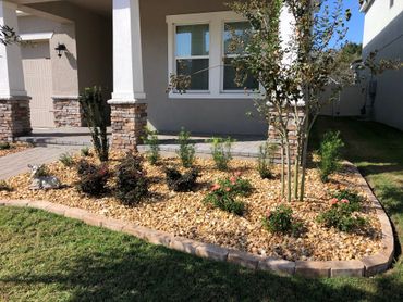 front of a home with a landscaped bed with pavers, rock, plants, and trees