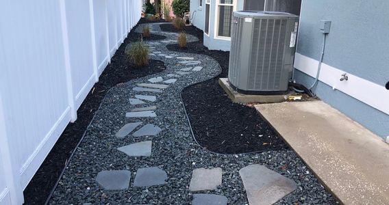 side of a home with various colors of rock divided by a barrier with pavers for walking