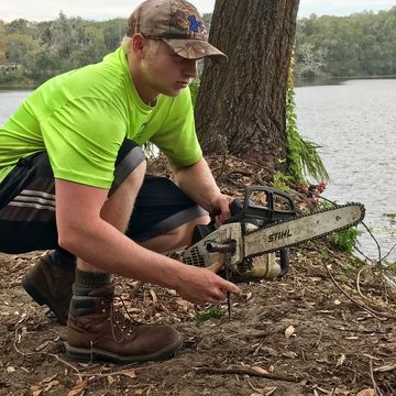 person kneeling by water with a chainsaw