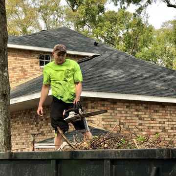 person standing in a dump trailer with a chainsaw cutting debris