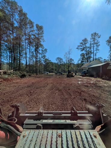 View from construction equipment clearing land near a rural house in a forested area.