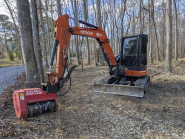 Orange Hitachi excavator with mulcher attachment in a wooded area.