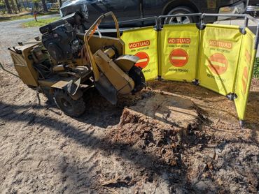 A stump grinder machine next to a large tree stump surrounded by caution barriers.
