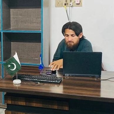 Man working at a desk with laptop and Pakistan flag.
