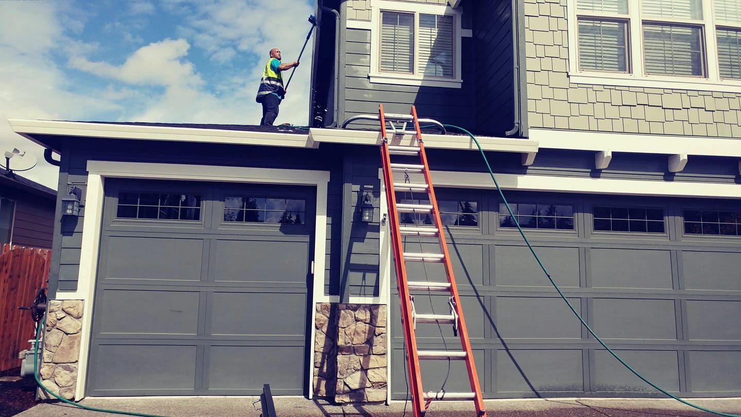 Man cleaning house gutters using a ladder and hose.