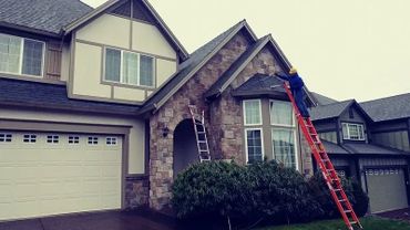 Worker on ladder painting a house exterior near the windows.