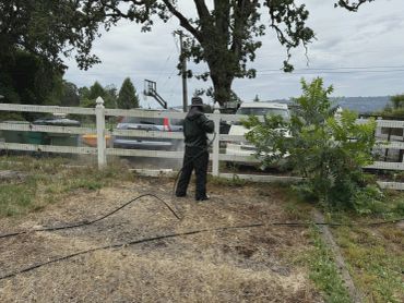 Person wearing protective gear using a hose near a fence.