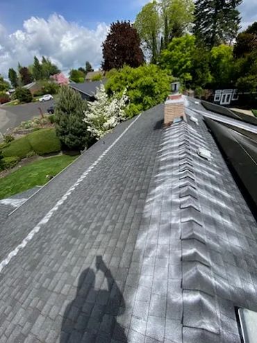 A rooftop with fresh and weathered shingles under a partly cloudy sky.