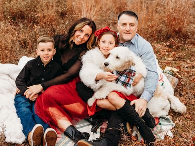 A happy family of four with their dog sitting on a blanket outdoors.