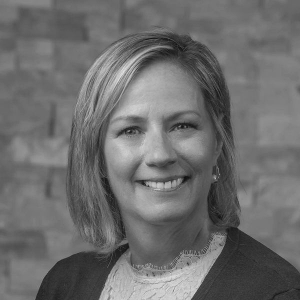 Smiling woman with blonde hair wearing a purple cardigan and white lace top.
