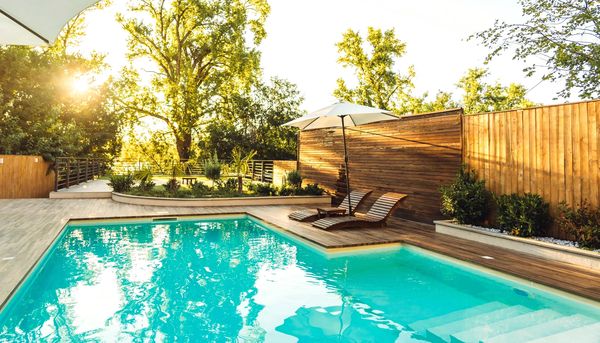 A serene backyard pool area with wooden loungers and umbrella in warm sunlight.