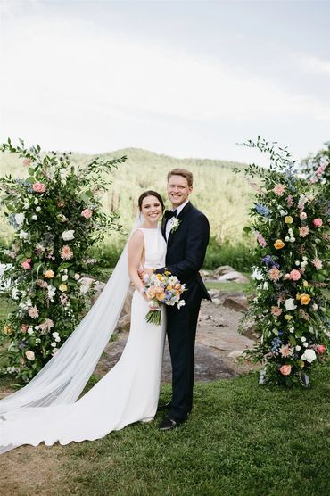 Newly Married Couple in front of an upright flower design by Twigs et fleurs. 