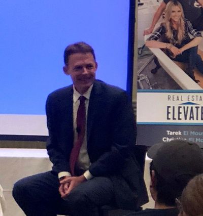 Man in a suit sitting during a presentation or event.