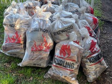 Bags of firewood and kindling stacked outdoors on grass.