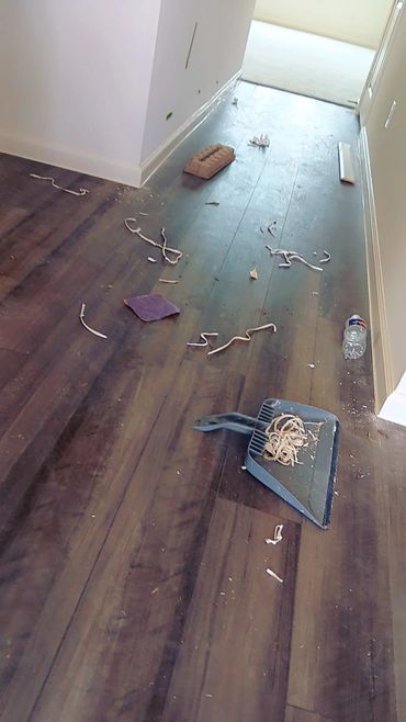 Messy floor with scattered debris, dustpan, and water bottle in a hallway.