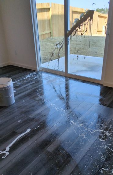 White paint spilled on dark hardwood floor and glass sliding door.