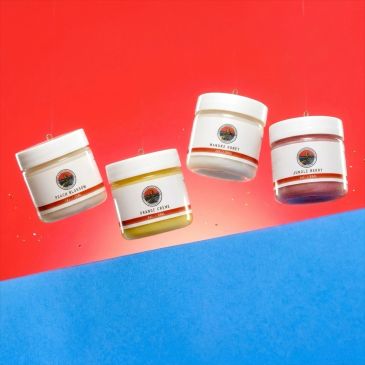 Four scented candles in white jars on a red and blue background.