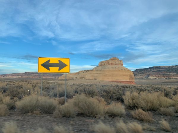 Yellow road sign with arrows pointing both left and right in a desert landscape.