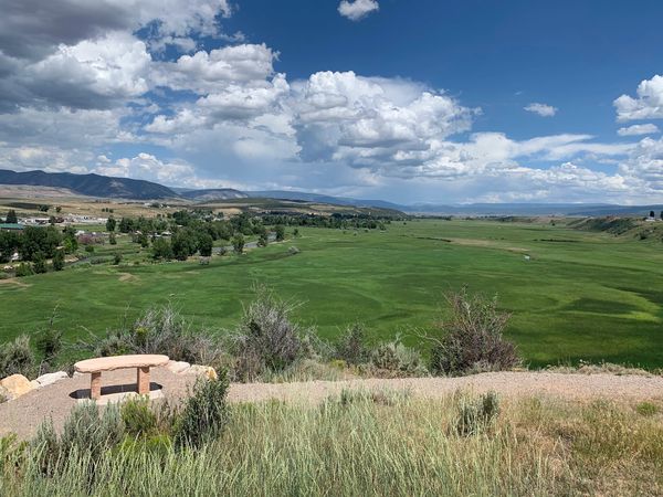 Bench overlooking a vast green valley under a partly cloudy sky.