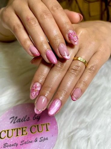 Elegant pink almond-shaped manicure with floral nail art and metallic accents at Cute Cut Beauty Salon & Spa