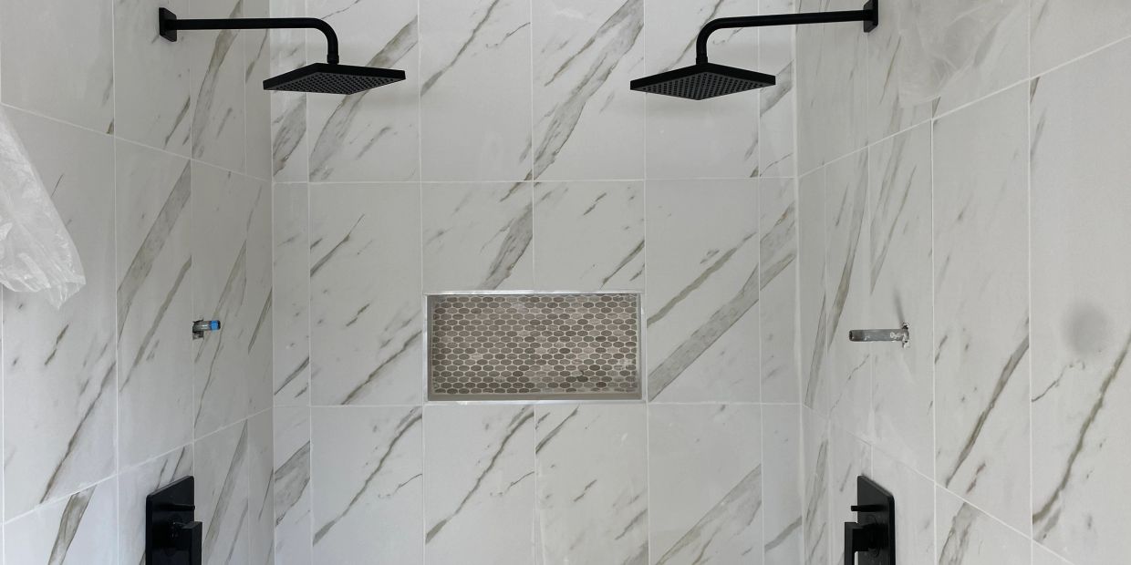 Modern dual showerheads in marble-tiled shower.