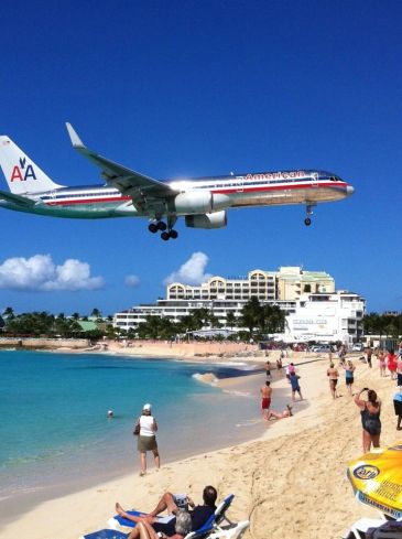 Airplane flying low over a beach with people watching.