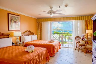 Hotel room with two orange beds and a scenic balcony view.
