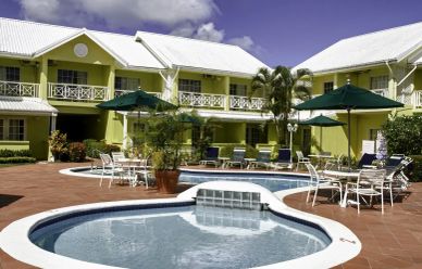 Outdoor pool area with tables, umbrellas, and a yellow building.