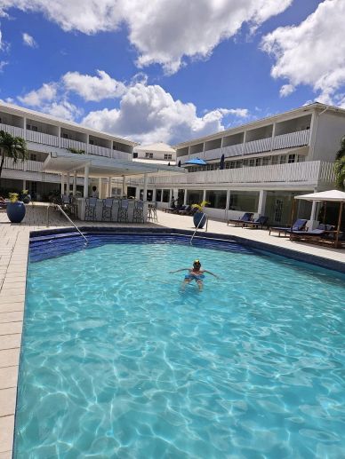 Person swimming in a clear hotel pool under a sunny sky.