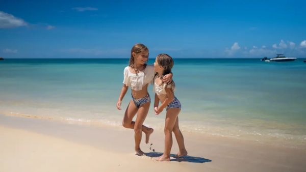 Two girls playing on the beach under a clear blue sky.