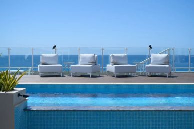 Four white chairs by a pool overlooking the ocean.