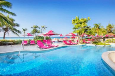 Sunny poolside with pink loungers and umbrellas by the beach.