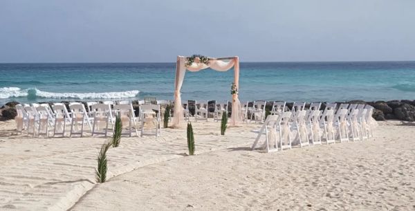 Beach wedding setup with white chairs and decorated arch.