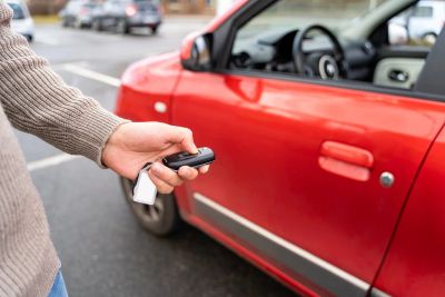Person holding car key near red car.