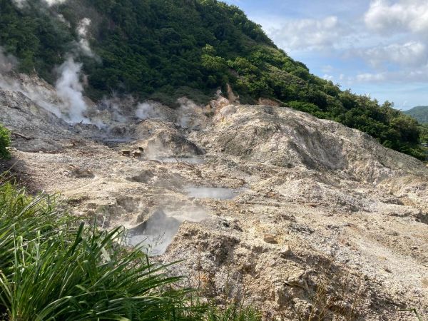 Steaming volcanic landscape with green hills.