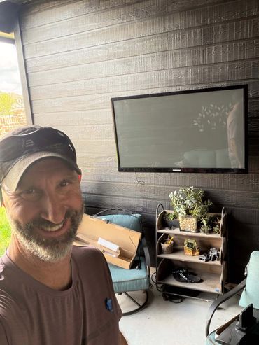 adam taylor the handyman hanging a tv on a back porch in alden bridge