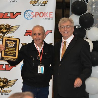 Two men at go-kart event, one holding an award plaque.