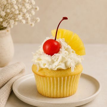 Pineapple cupcake with cherry and whipped cream.