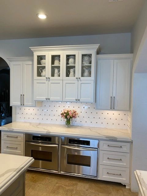 Custom white kitchen cabinets with glass-front upper cabinets and built-in double ovens.