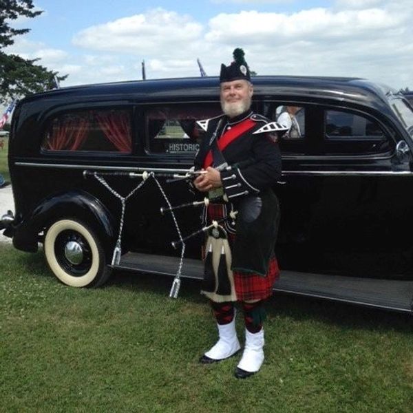 Iowa Bagpiper Ron Husted next to antique funeral coach.