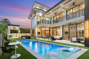 Modern luxury home with illuminated pool and outdoor seating at sunset.