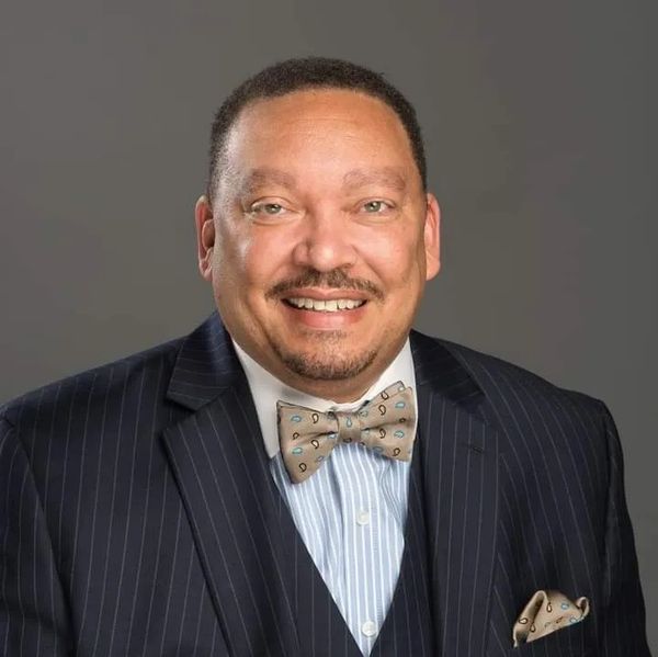 Smiling man in a pinstripe suit with a bow tie and pocket square.