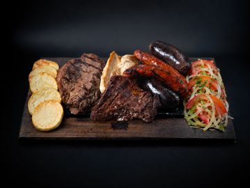 Grilled meat platter with sausages, steak, potatoes, and fresh salad.