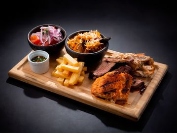 A wooden board with grilled chicken, fries, salad, and sauces.