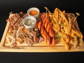 Wooden platter with assorted grilled meats and two dipping sauces.