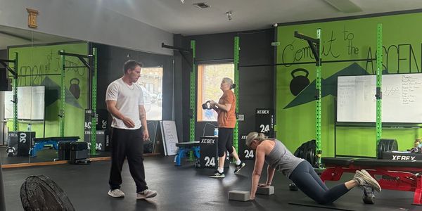 A woman exercises on the floor while two men observe in a gym.