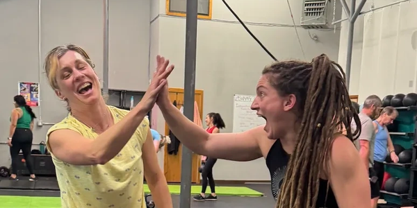 Two women happily high-fiving in a gym setting.