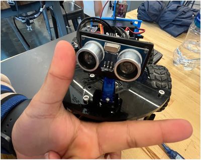 A small robot with sensors resembling eyes on a table, with a hand making a gesture in front.