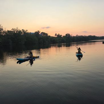 Two people kayaking on calm water at sunset.