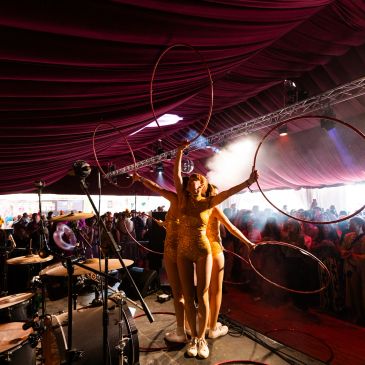 Performers with hoops entertain a crowd under a large tent with dramatic lighting.